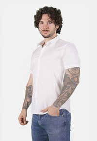 Camicetta bianca a maniche corte con colletto button-down e una tasca sul petto, abbinata a jeans blu; tessuto liscio con una vestibilità su misura.