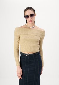 Beige averskuldret strikket crop topp med ribbing, paret med et høyt liv mørkt denim skjørt med synlige sømmer. Sorte solbriller og et fargerikt perlehalsbånd.