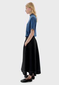 Haut bleu à manches courtes associé à une jupe noire longueur cheville avec une taille froncée et des coutures blanches. Des chaussures noires complètent la tenue.