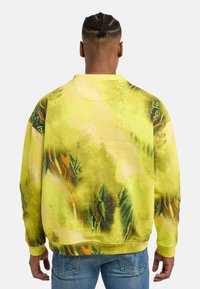 Gul sweatshirt med et tekstureret, abstrakt design, der har grønne og orange accenter. Løs pasform med ribbede manchetter og kant.