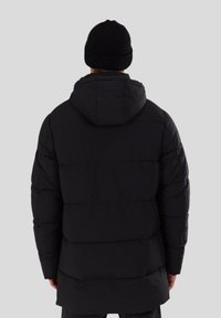 Schwarze Pufferjacke mit Kapuze, im gesteppten Design und geradem Schnitt, kombiniert mit einer schwarzen Strickmütze.