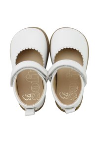 Zapatos de cuero blancos con bordes ondulados, puntera cerrada y correas en el tobillo. Las plantillas en un tono marrón claro presentan un lettering en relieve. Suelas planas.