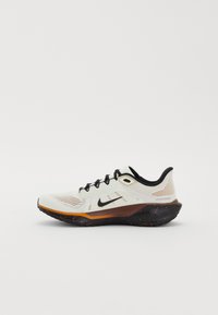 Chaussure de running Nike blanche et noire avec des accents orange, tige en mesh, lacets noirs et semelle noire mouchetée, vue de côté sur fond blanc.