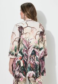 Lange mouw, losse top met een beige achtergrond en levendige bloemen- en luipaardprintpatronen. Zachte, gestructureerde stof en een gebogen zoom.