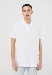 Polo bianco in cotone, con colletto classico, maniche corte e patta con tre bottoni. Tessuto liscio, vestibilità dritta.