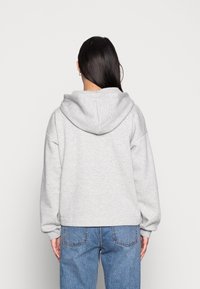 Sudadera con capucha en gris claro, de corte relajado, textura suave y hombros caídos, combinada con jeans de cintura alta en azul.