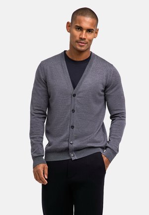 Grijze gebreide cardigan met een v-hals, zes knopen aan de voorkant, geribde manchetten en zoom, gedragen over een donker shirt en gecombineerd met donkere broeken.