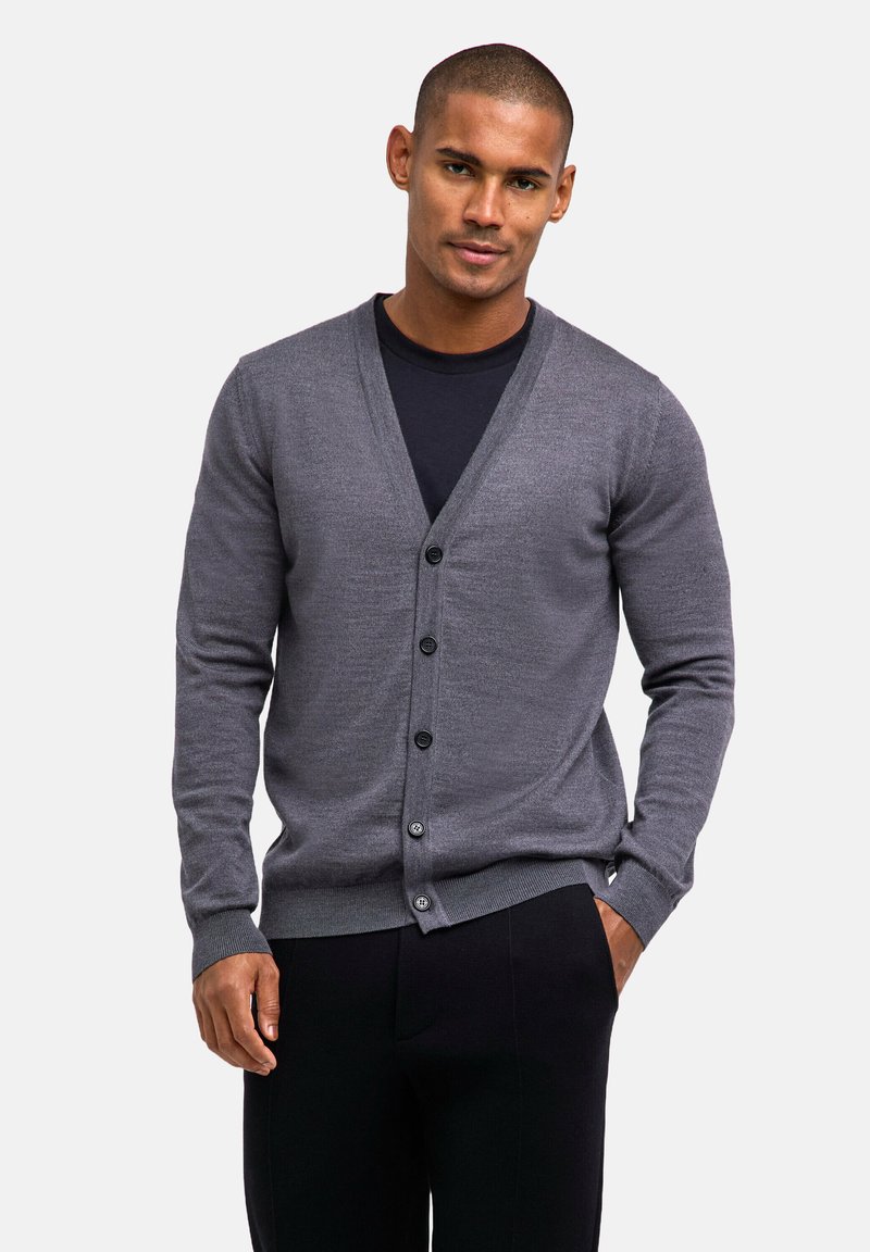 Grauer Strickcardigan mit V-Ausschnitt, sechs Knöpfen auf der Vorderseite, gerippten Bündchen und Saum, getragen über einem dunklen Shirt und kombiniert mit dunklen Hosen.