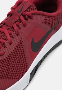 Rød mesh atletiksko med sorte accenter, tekstureret overdel og hvid mellemsål. Har snørebånd og et markant swoosh-logo på siden.