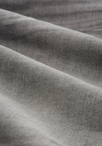 Grau gewobenes Gewebe mit einer strukturierten, gewebten Optik. Das Material zeigt subtile Farbnuancen, die die Tiefe seiner Oberfläche betonen.