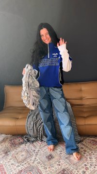 Kék versenystílusú ing fehér részletekkel és logóval; ezüst flitteres válltáska; világoskék farmernadrág nagy, szív alakú foltokkal.