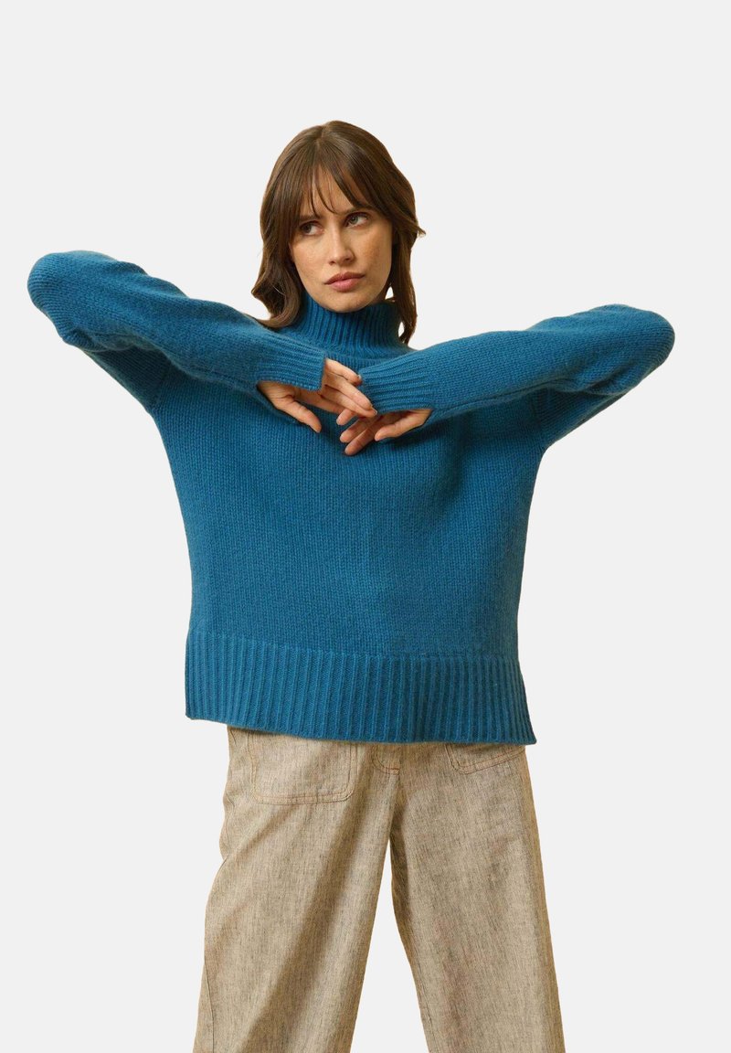 Przeciągający się sweter z wysokim kołnierzem w kolorze niebieskim, wykonany z fakturowanej dzianiny. Posiada długie rękawy z prążkowanymi mankietami oraz prążkowanym hemem.