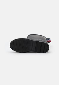 Botte en caoutchouc noire avec une semelle texturée, présentant un motif plat et strié, et une languette rouge, blanche et bleue à l'arrière.