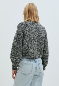 Grauer gestrickter, taillierter Pullover mit Ballonärmel, strukturiertem Finish und hohem Halsausschnitt, kombiniert mit hellblauen hochgeschnittenen Jeans.