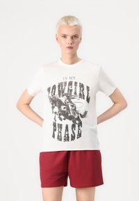 T-shirt en coton blanc à manches courtes, avec un texte graphique noir "EN PHASE COWGIRL" et une illustration d'un cowboy sur un cheval.