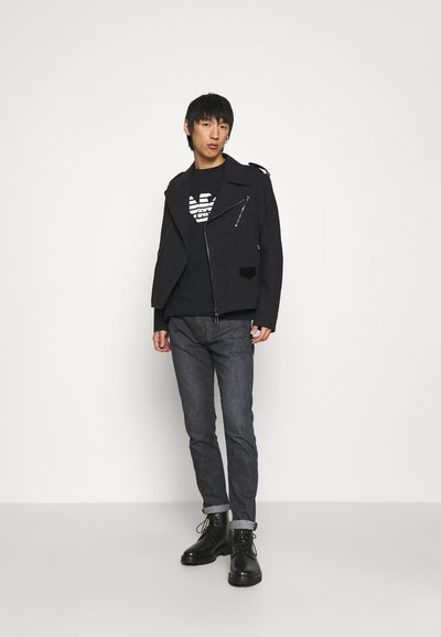 Black textured motorcycle jacket with zip details, worn over a black graphic t-shirt, paired with dark jeans and black lace-up boots.