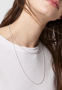 Cadenas de plata en capas alrededor del cuello, descansando sobre una camiseta blanca. Las cadenas tienen una textura suave y brillante y un diseño simple.