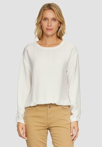 Witte lange mouwen top met een ronde halslijn en een gestructureerde stof, gecombineerd met lichtbruine broeken. Minimale ontwerp, ontspannen pasvorm.