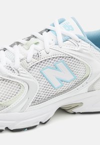 Vita och ljusblå träningssko med mesh-överkropp, snöre, vadderad krage och en stor "N"-logotyp på sidopanelen.