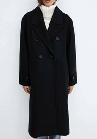 Cappotto nero doppiopetto con ampie rever, dettagli con bottoni e tasche laterali, realizzato in un tessuto testurizzato.