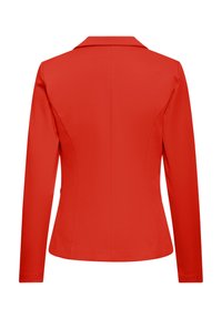 Set bagfra af en tætsiddende, langærmet rød blazer med en midtersøm og en klassisk krave på en hvid baggrund.