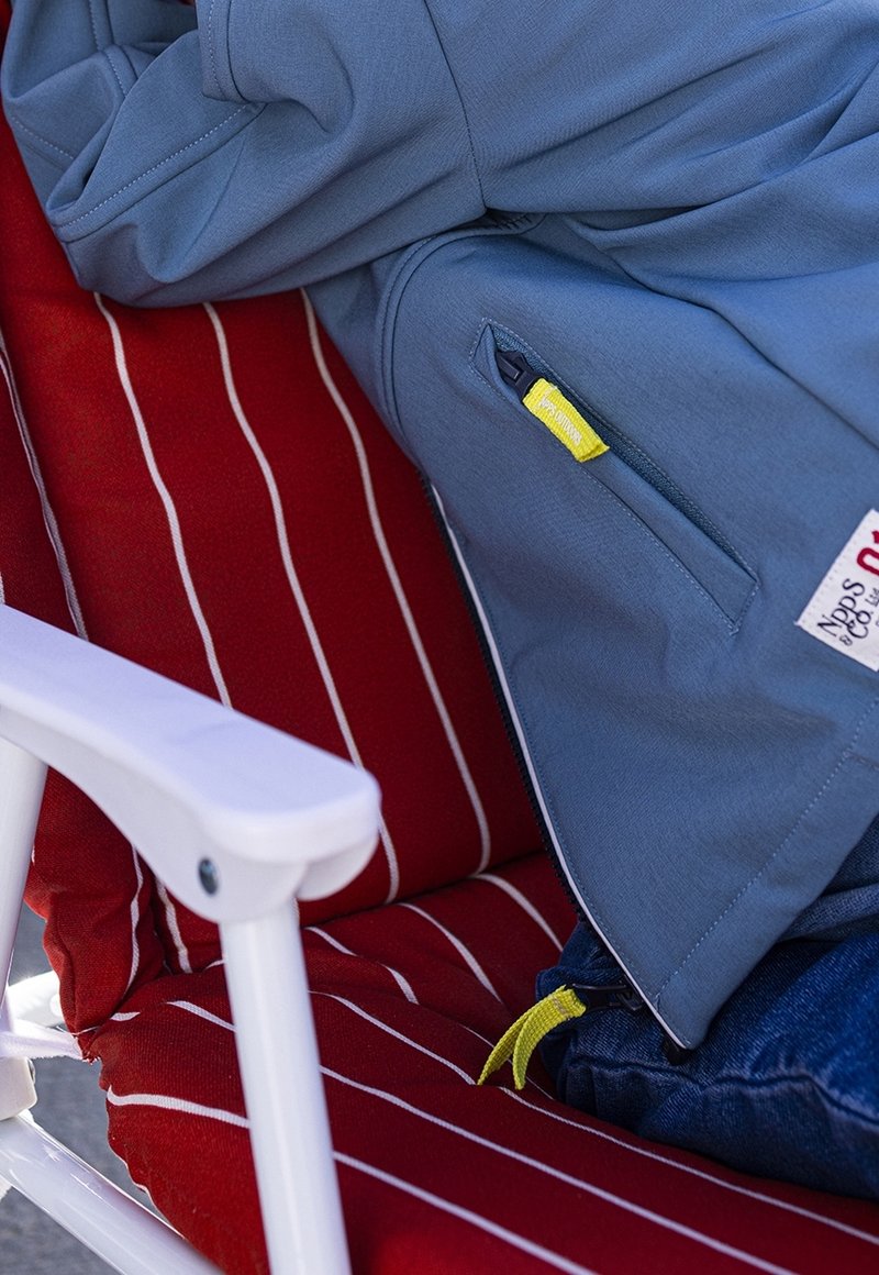 Light blue jacket with a zippered pocket; worn on a red and white striped chair. Features bright yellow zipper pull.