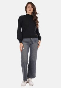 Maglione nero a maglia con collo alto, maniche a palloncino e polsini a coste; abbinato a jeans grigi a vita alta e sneaker bianche.