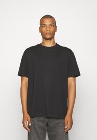 Czarny bawełniany t-shirt z okrągłym dekoltem, krótkimi rękawami i luźnym krojem. Noszony z szarymi dżinsowymi spodniami, minimalistyczny design, bez widocznych wzorów.