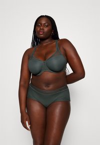 Dark green bra and matching high-waisted panties feature a textured pattern, mesh accents, and a small front closure detail.