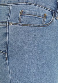 Ljusblå denimjeans med en liten bakficka, exponerad sömnad och detaljer i silvernitar. Tyget har en mjuk textur.