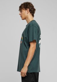 Mørkegrøn bomulds t-shirt med korte ærmer, der har et farverigt grafisk design på forsiden og tekst på bagsiden. Løs pasform.