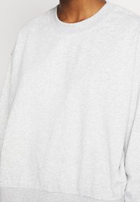 Sweatshirt gris clair en tissu doux, doté d'un col rond, d'une coupe décontractée et de poignets côtelés aux manches et à l'ourlet.