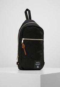 Zaino in tessuto nero con forma arrotondata, zip dorate, dettagli in pelle e patch con logo sulla parte anteriore. Include spallacci regolabili.