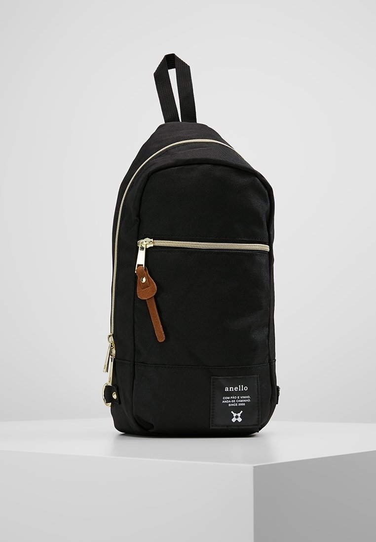 Zaino in tessuto nero con forma arrotondata, zip dorate, dettagli in pelle e patch con logo sulla parte anteriore. Include spallacci regolabili.