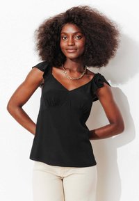 Haut sans manches noir avec un col en V, un détail froncé et des bretelles à volants. Tissu lisse et coupe ajustée.