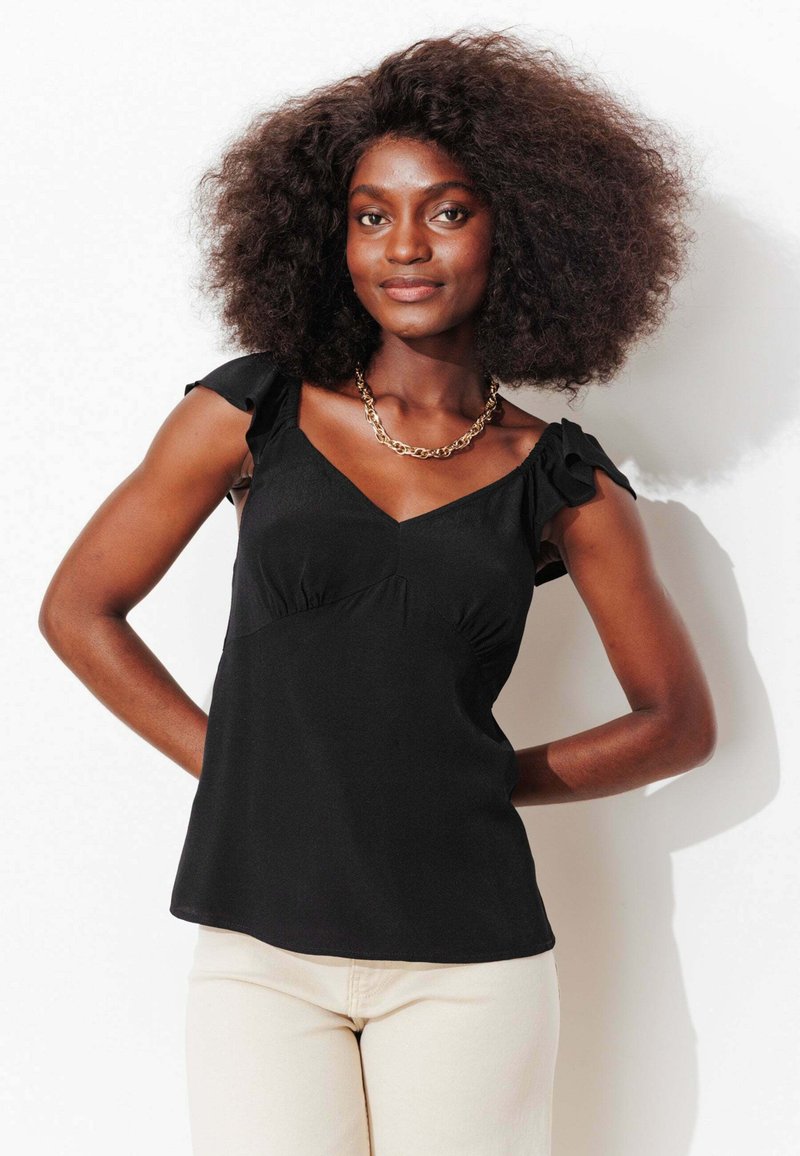 Haut sans manches noir avec un col en V, un détail froncé et des bretelles à volants. Tissu lisse et coupe ajustée.