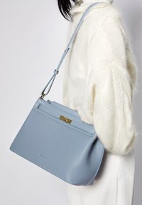 Ljusblå läderhandväska med en strukturerad form, utrustad med ett guldfärgat spänne och justerbar rem. Ytan har en texturerad finish.