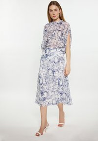 Chiffon-mekko, jossa on vaalea sininen kukkakuosi; väljät, lyhyet hihat; korkea kaulus; soljuva siluetti; yhdistetty valkoisiin nilkkaketjullisiin korkokenkiin.