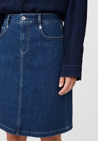 Jupe en denim bleu foncé à coupe droite, avec poches avant, passants pour ceinture et une fermeture avant par un seul bouton. Détails de coutures visibles.
