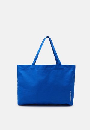 Jasně modrá obdélníková nákupní taška s dvěma uchy, s malým bílým potiskem v pravém dolním rohu.