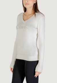 Witte gebreide trui met een V-hals, met een metallic logo "Guess est. 1981" op de borst en ribgebreide manchetten en zoom.