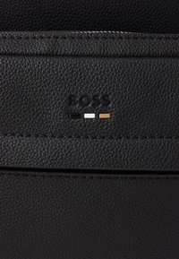 Fekete, texturált bőrtárca, amelyen a "BOSS" logó dombornyomott és három színárnyalat található: fekete, fehér és barna. Minimalista design, elegáns felület.