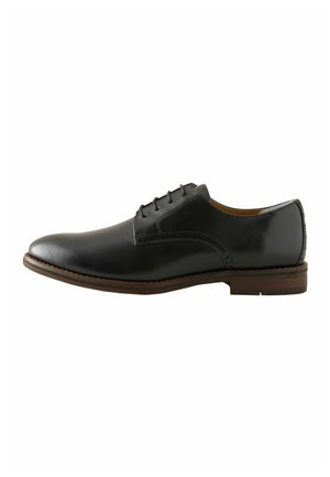 Zwarte leren heren oxford schoen met veters en bruine zool, zijaanzicht op een witte achtergrond.