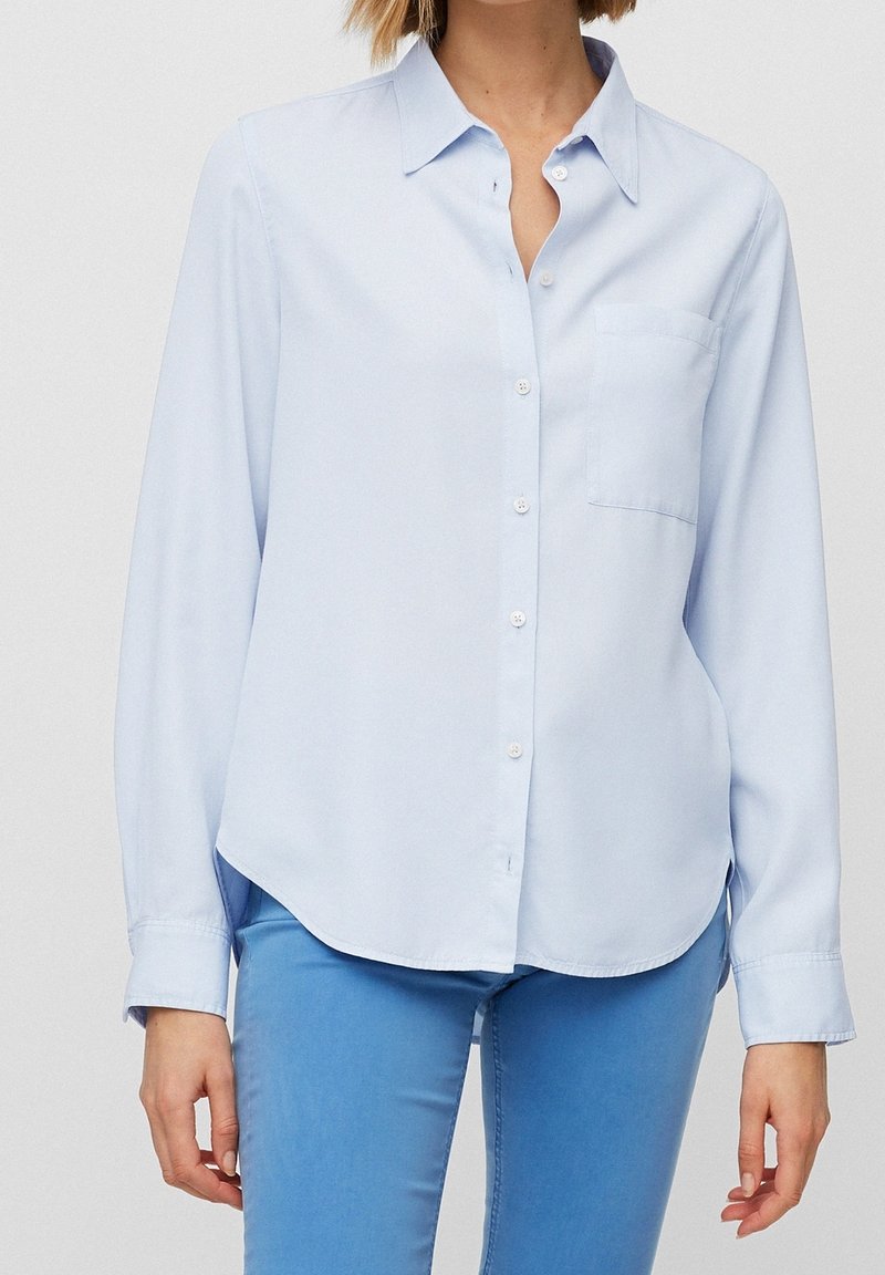 Light blue button-up shirt with long sleeves, a collar, and a chest pocket. Smooth texture with a slightly curved hem.