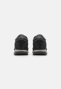 Chaussures de sport noires avec une tige en cuir lisse, des accents en daim, une semelle rembourrée, et une semelle intermédiaire grise texturée avec un détail de logo.