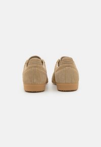 Béžové semišové tenisky s texturovaným povrchem, polstrovaným zadním dílem a gumovou podrážkou. Mají jemné prošívání a klasický nízký střih.