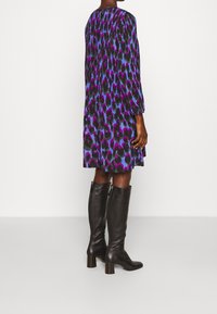 Langärmliges Kleid mit einem mehrfarbigen Tierdruck in Lila, Schwarz und Blau. Kombiniert mit knielangen schwarzen Lederstiefeln.