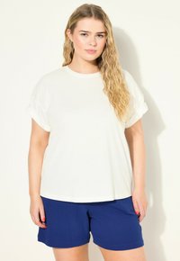 Wit T-shirt met opgerolde mouwen en een ontspannen pasvorm, gecombineerd met getextureerde marineblauwe shorts. Eenvoudig ontwerp, lichtgewicht materiaal en casual stijl.