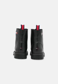 Stivali alla caviglia in pelle nera con punta arrotondata, dotati di un passante a strisce rosse e navy e di una patch con logo sul lato. Suola testurizzata per offrire aderenza.