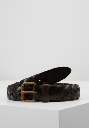 Ceinture en cuir tressé brun foncé avec une boucle en laiton, posée enroulée sur une surface blanche contre un fond clair uni.